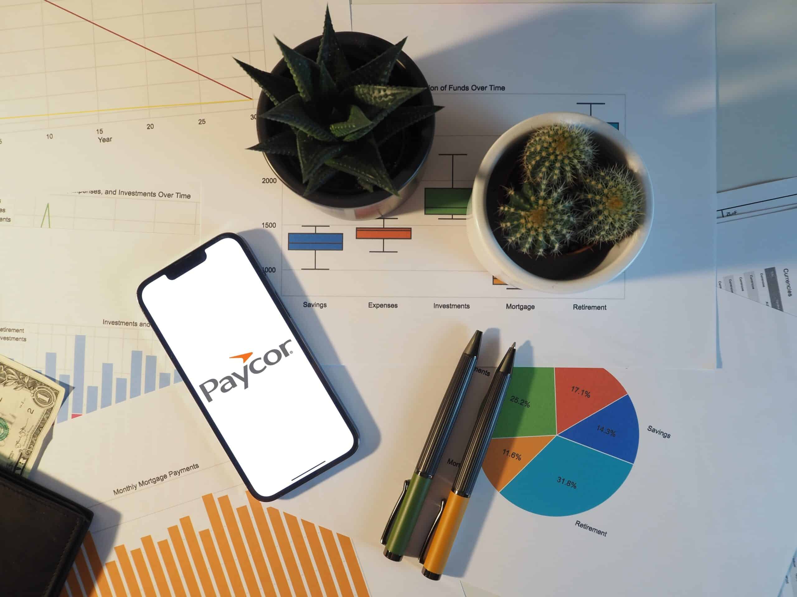 Shot of desk from above with mobile phone, pens, plants. Features Paycor logo